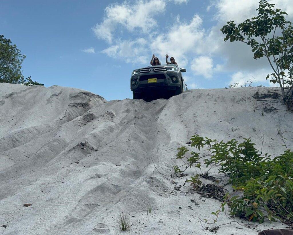 Terreinwagen op de rand van een witte zandduin onder een blauwe hemel