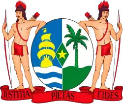 Het wapen van Suriname met twee inheemse figuren die bogen en pijlen vasthouden naast een schild. Op het schild staan een geel schip, palmboom, ster en een rode banier met de tekst Justitia Pietas Fides.