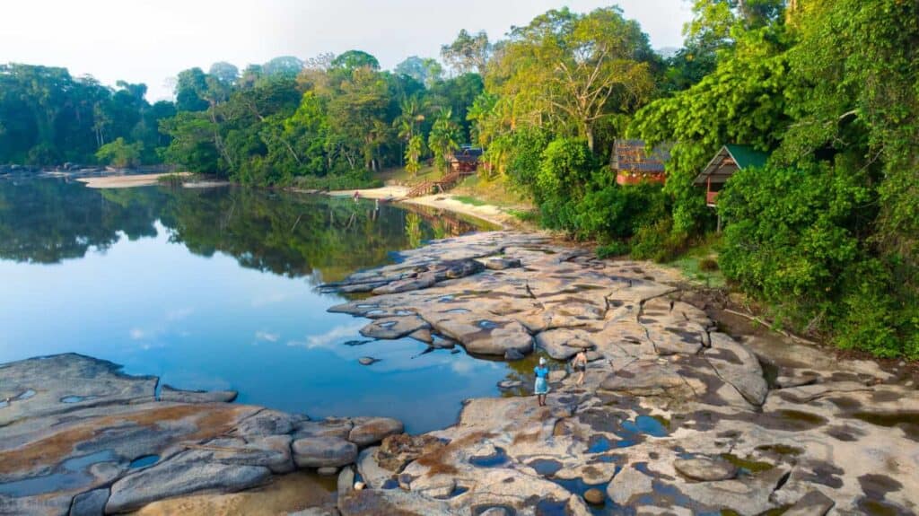 Danpaati River Lodge gezien vanaf de rivier, met rotsplaten en strand