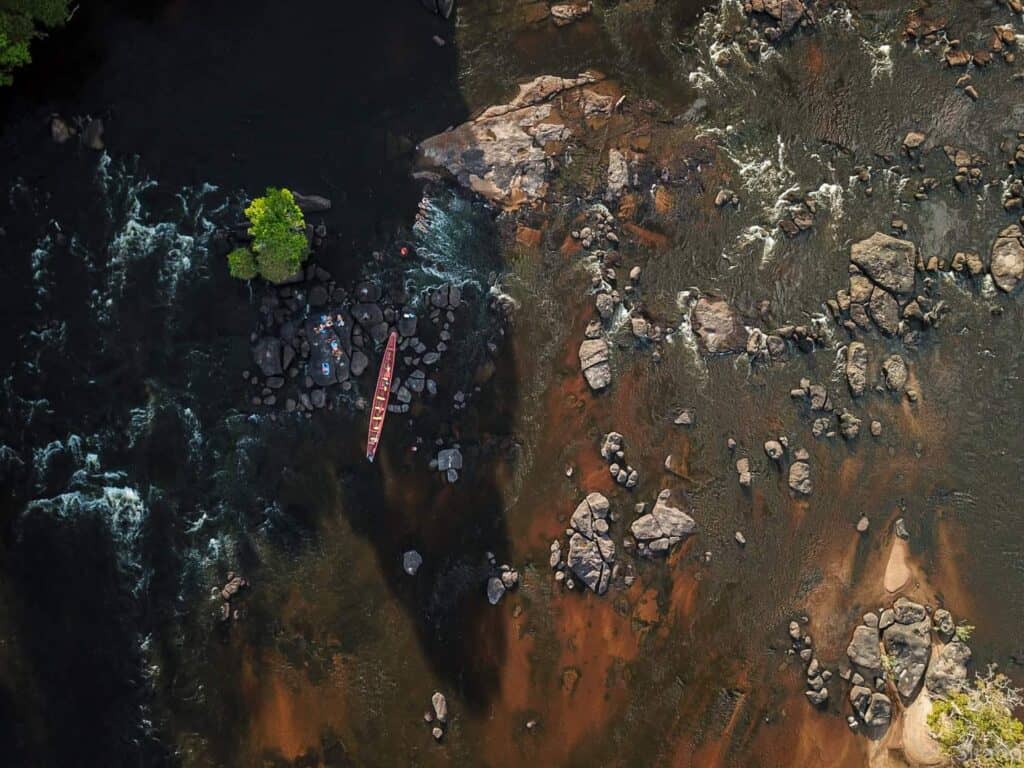 Luchtfoto van een sula (stroomversnelling) in de Boven-Suriname met korjaal