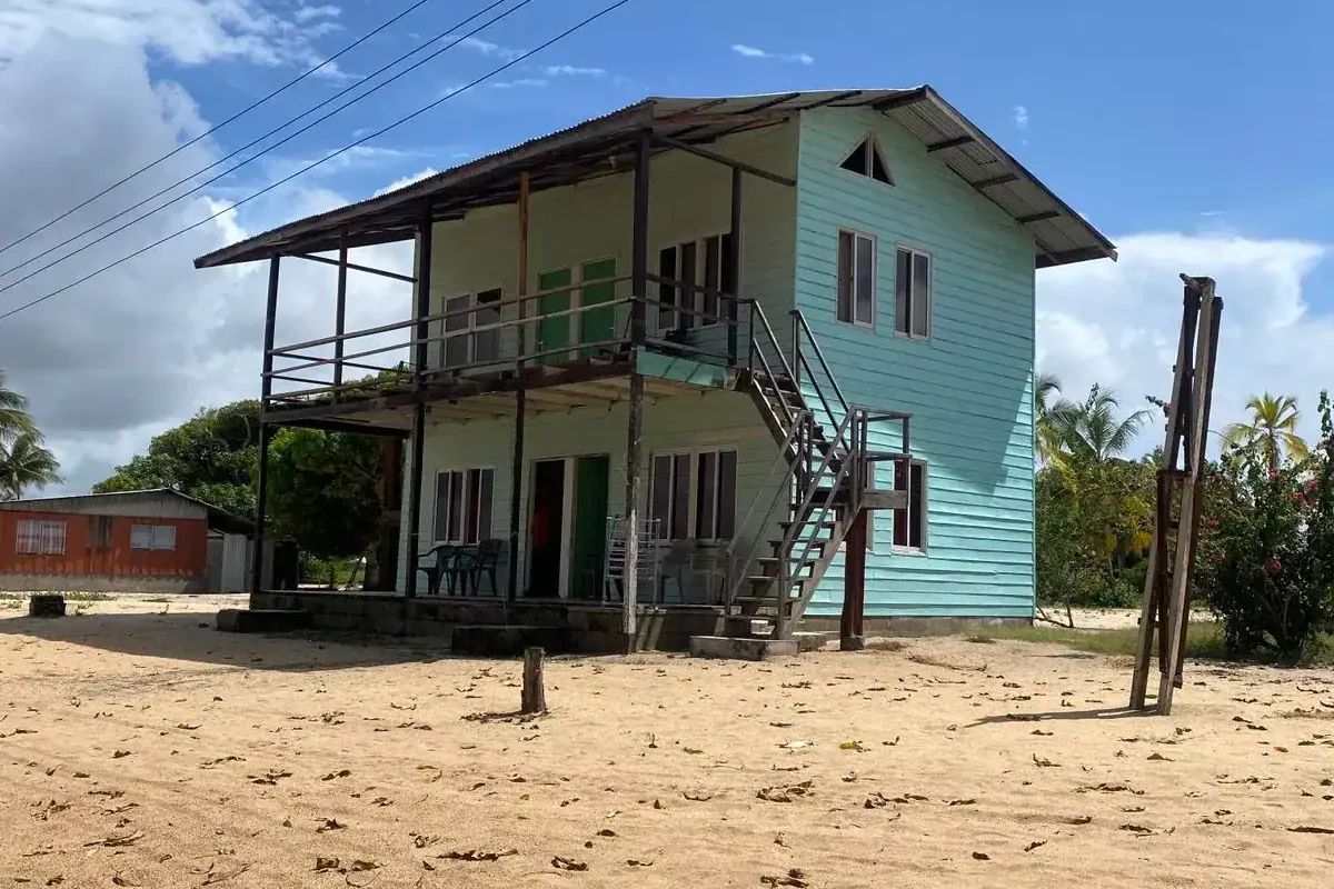 Turquoise houten lodgegebouw van Myrysji Lodge op het strand bij Galibi