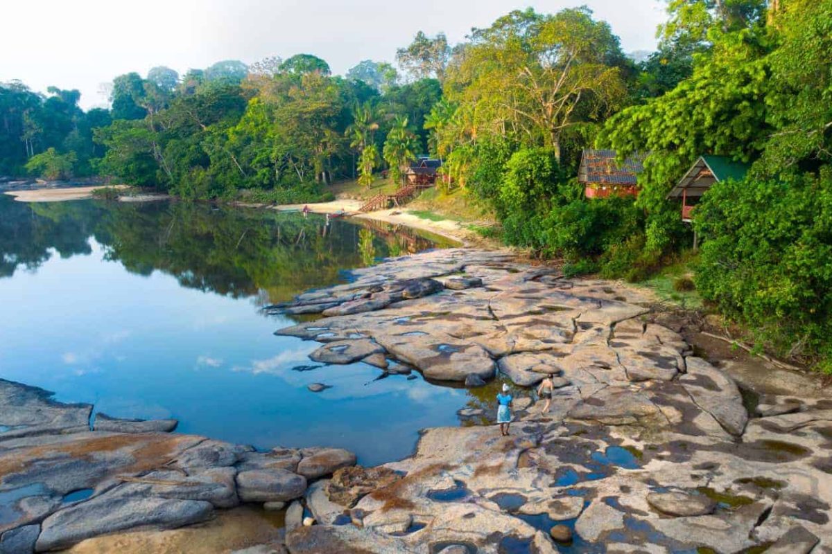 Danpaati River Lodge gezien vanaf de rivier, met rotsplaten en strand